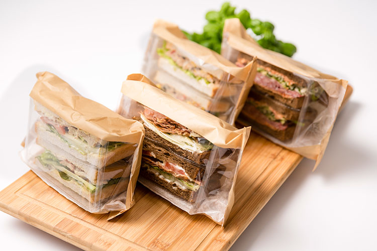 Verschiedene Sandwiches liegen verpackt auf einem Brettchen.